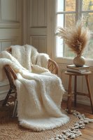 Cozy autumn reading nook with cream knitted blanket draped over wicker chair, pampas grass in ceramic vase, warm natural lighting through window.