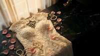 Elegant white lace wedding dress with golden jewelry rings scattered on dark marble surface with rose petals creating romantic bridal preparation scene.