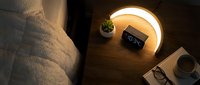 Cozy bedroom nightstand with glowing lamp, digital clock, coffee cup and plant creating warm ambient lighting for relaxation and sleep routine.