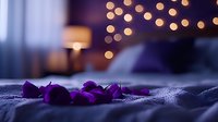 Purple rose petals scattered on bed with romantic bokeh lights creating intimate atmosphere for Valentine's Day or anniversary celebration.