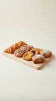 Assorted fresh pastries and baked goods on wooden cutting board including croissants, cinnamon rolls, and sweet breads for bakery display.