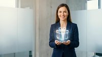 Businesswoman with long dark hair, Caucasian ethnicity, wearing navy blazer and white shirt, holding glowing digital shopping cart icon in modern office environment with glass partitions, representing e-commerce and online retail solutions.