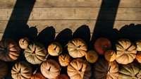 Autumn pumpkins arranged on rustic wooden deck with dramatic shadows creating seasonal harvest display for fall decorating and thanksgiving themes.