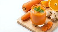 Fresh carrot orange ginger smoothie in glass with mint garnish on wooden board, healthy detox juice drink for wellness and nutrition lifestyle.