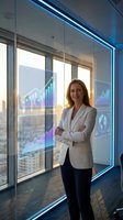 Confident businesswoman standing in modern office with holographic data charts and financial graphs displayed on smart glass windows.