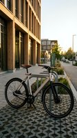 Modern fixed-gear bicycle parked on urban street with contemporary architecture, green charging station, and patterned pavement for sustainable city transportation and eco-friendly commuting concepts.