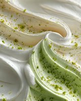 Creamy white meringue swirls with delicate green matcha powder sprinkled on top, creating a soft texture contrast for dessert decoration.