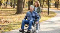 Mature Caucasian man in wheelchair with caring adult daughter walking together in autumn park with golden leaves on pathway for family bonding moments.