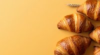 Fresh baked butter croissants arranged on warm yellow background with copy space, top view. French pastry breakfast composition for menu or food design.