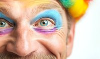 Close-up of Caucasian male with colorful face paint and rainbow wig making playful expression, perfect for entertainment or carnival themes.