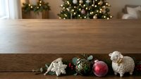 Wooden table with festive decorations including ornaments, sheep figurines, and greenery against blurred holiday lights background for seasonal marketing and home decor projects.