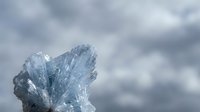 Clear ice crystal formation against dramatic cloudy sky background showcasing natural winter frost patterns and crystalline structures in cold weather conditions.