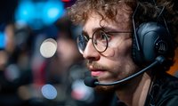 Young Caucasian male esports player with curly red hair and glasses wearing gaming headset in dark setting with blue bokeh lights, focused side profile view.