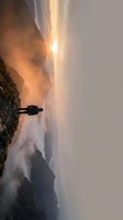 Silhouetted hiker standing on rocky mountain cliff at golden sunrise with misty valley below, adventure and exploration concept for travel and outdoor lifestyle imagery.