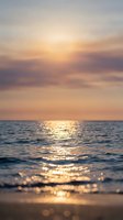 Serene ocean waves gently roll onto sandy shore during golden hour sunset, with warm sunlight reflecting across calm water surface and soft clouds above.