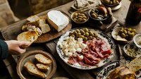 Mediterranean appetizer spread with prosciutto, cheese, olives, and crusty bread on rustic wooden table. Authentic antipasti platter for sharing at casual gathering.