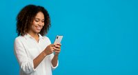 Young African American businesswoman using smartphone on bright blue background for mobile technology and communication concepts.