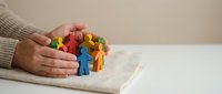 Protective hands covering diverse group of colorful wooden figures representing community support, teamwork and social unity concepts for business presentations.