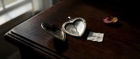 Open silver heart locket on dark wooden surface beside a sorry note and dried rose petal, evoking themes of regret, loss, and emotional healing.
