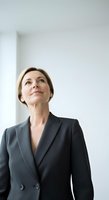 Middle-aged Caucasian businesswoman in dark blazer gazing upward with contemplative expression against white wall background for corporate and professional use.