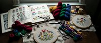Embroidery supplies with colorful threads, scissors, hoops and floral patterns on wooden table for needlework and handicraft projects.