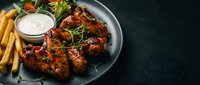 Grilled chicken wings with herbs and dipping sauce served alongside golden fries and fresh salad on dark plate for restaurant menu and food photography.