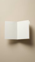 Blank folded greeting card mockup floating against a warm beige background, showing clean white paper with soft shadow for branding.