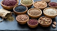 Assorted legumes and beans in wooden bowls on slate background with burlap sack. Variety of protein-rich pulses including lentils, chickpeas, kidney beans.