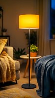 Modern floor lamp with yellow shade casting warm glow in cozy living room setting with throw blankets, houseplants and evening atmosphere.