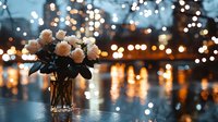 Delicate pink roses in glass vase against blurred bokeh lights background creating romantic evening atmosphere. Soft focus floral arrangement with water reflections.