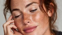 Young woman with freckles touching face in natural skincare beauty portrait showing healthy glowing skin and natural makeup look for wellness concepts.
