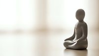 Minimalist meditation figurine in lotus position on wooden surface with soft natural lighting creating peaceful zen atmosphere for mindfulness and relaxation.