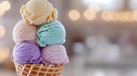 Colorful ice cream scoops stacked in waffle cone with pastel yellow, pink, mint, and purple flavors against blurred bokeh background.