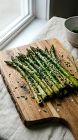 Grilled asparagus spears with herbs and seasoning on wooden cutting board near window for healthy cooking and meal preparation.