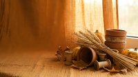 Rustic pottery vessels and wheat sheaves arranged on wooden surface near window with warm natural lighting creating cozy autumn harvest atmosphere.