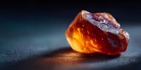 Glowing amber gemstone with warm golden light on dark textured surface creating dramatic atmospheric lighting for luxury jewelry and precious stone concepts.