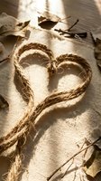 Rustic rope heart shape on burlap fabric with dried autumn leaves in warm sunlight for romantic crafts and seasonal decorations.