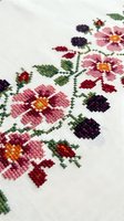 Traditional cross stitch embroidery with pink flowers and berries on white linen fabric. Handmade needlework craft showcasing colorful floral pattern.