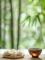 Steaming dumplings and hot tea on bamboo mat with blurred green bamboo forest background, creating serene Asian dining atmosphere.