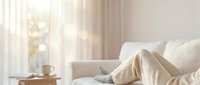 Cozy bedroom interior with soft morning sunlight streaming through sheer curtains, unmade bed with cream bedding, peaceful atmosphere for home decor.