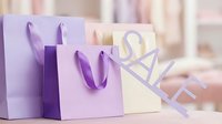 Pastel purple and beige shopping bags with sale sign in soft boutique setting, perfect for retail promotion and seasonal discount concepts.