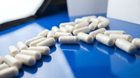 White pharmaceutical capsules scattered on blue surface with medical equipment in background for healthcare and medicine concepts.