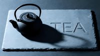 Cast iron teapot on dark slate board with engraved TEA lettering, dramatic shadow, moody blue tones for cafe menu or tea brand design.