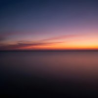 Serene ocean sunset with vibrant purple and orange sky reflecting on calm water surface creating peaceful seascape horizon for meditation backgrounds.