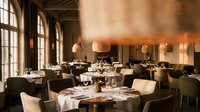 Elegant upscale restaurant interior with warm lighting, white tablecloths, modern chairs and large windows creating sophisticated dining atmosphere.