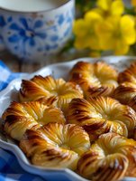 Golden puff pastry rings with flaky layers arranged on white plate beside floral teacup and yellow flowers for breakfast or tea time serving.