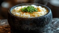 Steaming hot rice porridge topped with fresh green onions and spices served in traditional stone bowl. Asian comfort food with aromatic garnish.