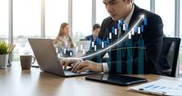 Young businessman analyzing financial data on laptop with digital growth chart overlay in modern office environment for business analytics presentations.