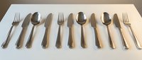 Elegant stainless steel cutlery set with forks, knives and spoons arranged in row on white surface. Modern kitchen utensils for dining and food service.