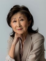 Elegant mature Asian woman in beige blazer poses thoughtfully with hand on chin against light background, expressing confidence and wisdom through gentle smile.